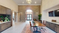 Located at 4775 Dublin Road in Columbus, Ohio, this single-story community amenity facility offers a thoughtfully designed layout encompassing a fitness center, kitchen, entrance, hallway, and recreational spaces. The entrance greets visitors with soaring ceilings clad in light wood paneling, large windows that flood the space with natural light, and a built-in media niche flanked by greenery, creating a warm and welcoming atmosphere. The kitchen is a standout feature, showcasing rich terracotta-toned cabinetry with decorative glass-front uppers, a brick-tile backsplash, stainless steel appliances, and a granite-topped island with seating — all beneath vaulted ceilings with exposed wood beams and a globe pendant chandelier. Outdoor views of the community pool are visible through expansive windows. The fitness facility spans two exercise rooms equipped with cardio machines, cable strength equipment, free weights, and stability gear, all set on durable flooring under vaulted, beam-accented ceilings with craftsman-style pendant lighting and large windows providing ample natural light. Large wall mirrors enhance the sense of openness throughout. A billiards and lounge area rounds out the space, featuring a full-size pool table, comfortable seating, a wall-mounted TV, and whitewashed shiplap walls beneath dramatic vaulted ceilings — ideal for relaxation and recreation.