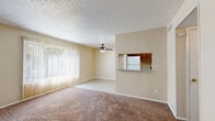 This single-floor residence offers a practical and comfortable layout with well-defined living spaces. The open living and dining area is a standout feature, finished with plush carpet and light wood-look flooring near the entryway. A ceiling fan with integrated lighting anchors the living room, while a large sliding glass door dressed with vertical blinds fills the space with natural light and provides outdoor access. A pass-through opening connects the living area to the kitchen, enhancing the open feel. The kitchen is well-appointed with warm wood cabinetry, granite-style countertops on both sides, a gas range, and light wood-look flooring for easy maintenance. A white refrigerator and built-in appliances complete the functional layout. The bedrooms are carpeted and generously sized, each offering closet storage. One bedroom features a spacious walk-in closet with a central built-in shelving unit flanked by dual hanging rods, providing excellent organization. Another bedroom includes a standard sliding-door closet. An electrical panel is conveniently accessible within the unit. Textured ceilings are consistent throughout, and neutral warm beige tones lend a cohesive, inviting ambiance across all rooms.