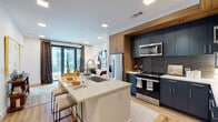 Located at 1150 Spring St NW in Atlanta's vibrant Midtown neighborhood, this single-floor residence showcases a thoughtfully designed open-concept layout with contemporary finishes throughout. The kitchen serves as a central focal point, featuring bold navy-blue cabinetry accented by warm wood trim that frames the cooking area. A textured dark tile backsplash adds depth behind the stainless steel appliances, which include a gas range, built-in microwave, and French door refrigerator. A substantial island with a white quartz countertop and an integrated sink offers casual seating and additional workspace, flowing naturally into the adjacent living area. Light wood-tone flooring runs throughout the main living spaces, enhancing the bright, airy atmosphere created by recessed lighting. The living area connects to floor-to-ceiling windows and sliding glass doors that frame dynamic urban views of the Atlanta skyline. The bedrooms continue the modern aesthetic, each benefiting from large windows and balcony access that flood the rooms with natural light. The bathroom features a sleek, dark-cabinetry vanity, light wood flooring, and crisp white walls, maintaining the residence's cohesive contemporary style.