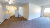 This single-floor, 2-bedroom, 1-bathroom unit is thoughtfully laid out to maximize comfort and functionality. The main living area features wall-to-wall carpeting and a neutral color palette, creating a bright and open atmosphere. Smooth, light-toned walls complement the textured ceiling throughout, lending the space a clean, understated aesthetic.

The galley-style kitchen is efficiently designed with ample white cabinetry both above and below the countertops, providing generous storage. Dark hardwood-style flooring grounds the space, contrasting neatly with the white appliances, including a refrigerator, range, and dishwasher. A single-basin sink sits beneath upper cabinets, completing the practical layout.

The bedrooms are carpeted and well-proportioned. A standout feature is the sliding glass door that opens directly onto a private balcony, offering outdoor views of surrounding greenery and neighboring structures — an ideal spot for fresh air and natural light. Vertical blinds accompany the sliding door, allowing for adjustable privacy and light control.

A hallway connects the main living areas to the bedrooms and bathroom, ensuring a logical and comfortable flow throughout the unit. Overall, this space combines practicality with comfortable, everyday livability.