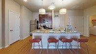 Located at 504 E Ninth St in Tucson, Arizona, this single-floor unit offers a well-designed, functional layout ideal for comfortable everyday living. The kitchen serves as a central highlight, featuring rich dark wood cabinetry, granite countertops, stainless steel appliances — including a refrigerator, stove, and microwave — and a spacious breakfast bar with pendant lighting overhead, making it equally suited for casual dining and entertaining. Hardwood-style flooring runs throughout the main living areas, adding warmth and continuity to the space. The living room provides a comfortable retreat with natural light streaming in through slatted windows. Multiple bedrooms are carpeted for added comfort, with at least one bedroom offering a walk-in closet for generous storage. Each bedroom benefits from natural light through well-positioned windows. Two full bathrooms mirror each other in design, each appointed with dark wood vanities, granite countertops, hardwood-style flooring, and a full bathtub with shower combination. The neutral warm-toned walls throughout create a cohesive, inviting ambiance. The overall layout, as seen in the overhead dollhouse view, flows efficiently between the kitchen, living, and private sleeping quarters.