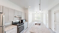 Located at 2817 Andover St in Jefferson, Louisiana, this two-bedroom, one-bathroom unit offers a thoughtfully designed single-floor layout with contemporary finishes throughout. The open kitchen serves as the heart of the home, featuring a central island with granite countertops and a built-in sink, gray shaker-style cabinetry, stainless steel appliances including a refrigerator, range, and microwave, and stylish pendant lighting overhead. Light wood-style flooring runs seamlessly throughout the entire unit, creating a clean, cohesive aesthetic. The living and dining area adjoins the kitchen and benefits from a ceiling fan and a large window that brings in abundant natural light with views of the surrounding greenery. Both bedrooms are bright and airy, each equipped with ceiling fans and generously sized windows that frame outdoor views. The primary bedroom offers a comfortable sense of space and privacy. The bathroom is well-appointed with a granite-topped vanity, gray cabinetry, a framed mirror, and accessibility grab bars. Crisp white walls and recessed lighting throughout the unit contribute to an overall clean, modern ambiance that is both functional and inviting.