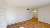 Located at 299 Kingspoint Dr in El Paso, TX, this single-floor, one-bedroom, one-bathroom unit offers a well-organized layout across a compact yet functional floor plan. The living room is a bright and inviting space, highlighted by warm wood-look flooring, white painted stone accent walls, and a large sliding glass door fitted with vertical blinds that floods the room with natural light. Adjacent to the living room, the dining area continues the wood-look flooring and features a standout white painted stone accent wall paired with a classic brass chandelier, adding a touch of character to the space. The galley-style kitchen is efficiently designed with white cabinetry, dark countertops, a double sink, and white appliances, including a full-size refrigerator. A window at the end of the kitchen brings in additional natural light. The generously sized bedroom is carpeted and features its own white painted stone accent wall flanked by two windows. A walk-in closet with dual shelving and hanging rods provides ample storage. The bathroom includes a tub-shower combination with white tile surround and wood-look flooring. Two hallways connect the spaces seamlessly, completing this well-appointed single-level home.