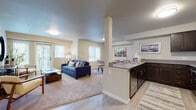 This single-floor residence is designed with an open-concept layout that seamlessly connects the kitchen, dining, and living areas. The kitchen is well-appointed with dark espresso cabinetry, stainless steel appliances including a refrigerator, range, and microwave, and a peninsula countertop with seating that serves as both a workspace and casual dining area. Light wood-style flooring runs throughout the kitchen, transitioning to plush carpet in the living and dining spaces.

The living room is bright and welcoming, featuring multiple windows fitted with vertical blinds and a sliding glass door that opens to a private balcony with outdoor views. The adjacent dining area provides a defined space for formal meals and benefits from additional natural light through its own window.

Both bedrooms are carpeted and sized to comfortably accommodate standard furniture. The primary bedroom includes a walk-in closet and is brightened by a window overlooking the exterior. The secondary bedroom similarly features a window and plush carpeting. The bathroom offers a vanity with dark cabinetry, an undermount sink, and light wood-style flooring, maintaining the cohesive neutral palette found throughout the residence.