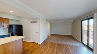 This single-floor residence offers a well-organized, open layout that seamlessly connects the main living areas. The living room is a standout space, featuring a tile-surround fireplace as a central focal point, crown molding along the ceiling, and a large sliding glass door that opens to a private balcony, flooding the room with natural light and offering views of lush surrounding greenery. The flooring transitions between warm hardwood in the main living and kitchen areas and plush carpet in the lounge portion of the living space, adding texture and comfort underfoot.

The kitchen is designed for functionality, featuring warm oak cabinetry that extends to the upper walls for generous storage, a peninsula with a clean white countertop that provides additional workspace and separates the kitchen from the living area, and a full suite of black appliances including a range, built-in microwave, dishwasher, and refrigerator. A stainless steel sink with a window nearby completes the practical layout.

The bathroom is finished with warm wood vanity cabinetry topped with a white countertop and single basin sink, a large frameless mirror with elegant overhead lighting, tile flooring, and a separate shower and toilet area. Crown molding throughout the main living spaces and textured ceilings contribute to the cohesive, classic character of this well-appointed residence.