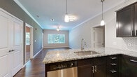 Located at 401 N Forest Ave in Liberty, Missouri, this single-story, two-bedroom, one-bathroom residence offers a thoughtfully designed layout with contemporary finishes throughout. The open-concept kitchen and living area forms the heart of the home, creating a cohesive and functional space for daily living. The kitchen is outfitted with dark espresso cabinetry, granite countertops, a stainless steel appliance suite including a range, microwave, dishwasher, and refrigerator, and a central island with a undermount sink. A geometric tile backsplash and pendant lighting add refined detail to the space. The adjoining living room features hardwood-style flooring, crown molding, a ceiling fan, and a large window that draws in natural light and outdoor views of surrounding greenery. Both bedrooms offer ceiling fans and generous natural light via wide windows; the primary bedroom includes a walk-in closet, while the second bedroom features carpet flooring. The bathroom is finished with a dark vanity, granite countertop, a large mirror, and a full tub-shower combination. Consistent neutral-toned walls and crown molding unify the overall aesthetic of the home.