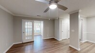 Located at 2410 Allerton Way in Charlotte, NC, this one-bedroom, one-bathroom home offers a well-designed single-level layout with a cohesive, neutral color palette and hardwood-style flooring throughout. The open living area is accented with crown molding, a ceiling fan, and a charming French door that connects to a sunlit bonus room — ideal as a sitting area or office — featuring large windows that invite abundant natural light and outdoor views. The kitchen is thoughtfully equipped with white shaker-style cabinetry, white quartz countertops, a stainless steel sink, and black appliances including a range, microwave, and dishwasher. A dedicated laundry area accommodates a full-size washer and dryer with additional shelving for storage. The spacious bedroom includes a ceiling fan, a natural-light window, and a built-in shelving unit, complemented by two closets for ample storage. The bathroom features a wide vanity with white cabinetry and quartz countertop, a large framed mirror, and a shower-tub combination. Throughout the home, clean white trim, neutral gray walls, and consistent flooring create a bright, move-in-ready atmosphere.