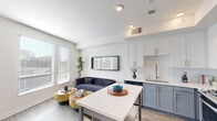 This thoughtfully designed one-bedroom, one-bathroom unit offers a smart and stylish layout across a single floor. The open-concept living and kitchen area anchors the space, where light wood-look flooring, neutral white walls, and recessed lighting create a clean, contemporary atmosphere. The kitchen features white upper cabinetry, grey lower cabinets, a marble-look countertop island with bar seating, stainless steel appliances including a dishwasher, and a single-basin sink — all seamlessly integrated into the living area. The living room is bright and airy, with two large windows fitted with horizontal blinds that invite natural light and offer views of surrounding greenery. A connecting hallway leads to the private bedroom, a cozy and well-proportioned retreat featuring wood-look flooring, crisp white walls, and ample space for a full-size bed. The bathroom is finished in a clean, all-white palette with subway tile surrounding a full soaking tub and shower combination, complemented by chrome fixtures and a vanity with storage. The unit's cohesive modern design, efficient use of space, and quality finishes make it a comfortable and functional living environment.