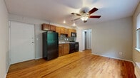 Located at 558 Lowell Ave in Cincinnati's 45220 neighborhood, this one-bedroom, one-bathroom unit offers a practical and well-appointed layout across a single floor. The open living and kitchen area features warm hardwood flooring and is anchored by a ceiling fan with integrated lighting. The kitchen is efficiently designed with rich wood cabinetry, a mosaic tile backsplash, stone-look countertops, and a full suite of black appliances including a refrigerator, gas range, built-in microwave, and dishwasher. A hallway connects the main living area to the private quarters of the unit. The bedroom is carpeted for comfort and receives natural light through a window overlooking lush greenery outside. A reach-in closet with built-in shelving provides organized storage. The bathroom is finished with neutral tile flooring and features a glass-enclosed walk-in shower with stone-tiled surround, complemented by a window that brings in natural light. A lighted vanity mirror completes the space. Overall, the unit offers a functional and cohesive design suited for comfortable everyday living.
