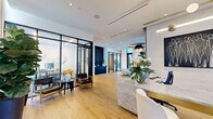 Located at 777 Northwest 2nd Avenue in Miami, FL, this single-floor commercial space delivers a refined, contemporary aesthetic across a well-appointed layout. Light oak hardwood flooring runs throughout, anchoring a cohesive design that balances openness with defined functional zones.

The welcoming reception area centers on a striking marble desk with gold accents, paired with cream upholstered chairs and an elegant sputnik-style pendant light. Floor-to-ceiling sheer curtains filter abundant natural light from expansive windows, creating a bright and airy atmosphere.

The living/lounge area features a bold navy textured accent wall alongside a sleek credenza, offset by a dramatic drum-shaped pendant chandelier overhead. Curved sofas and accent chairs form an inviting seating arrangement, while lush indoor plants add organic warmth throughout the space.

Glass-walled, black-framed office enclosures provide privacy without sacrificing visual connectivity. One office is furnished with a dark marble-top conference table and cognac leather chairs, accented by vibrant curated artwork. A second private office accommodates a dedicated workstation with yellow accent seating.

The hallway transitions seamlessly between zones, maintaining the space's clean, modern flow. Every detail — from the sculptural light fixtures to the carefully selected art pieces — reflects a polished, design-forward sensibility suited to a premium professional environment.