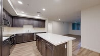 Located in Oxnard, California, this well-appointed single-floor residence offers four bedrooms and two full bathrooms within a generously sized floor plan. The open-concept kitchen and living area serves as the heart of the home, showcasing rich dark cabinetry, bright white countertops, stainless steel appliances including a refrigerator, range, microwave, and dishwasher, and a central island with recessed lighting above. Light wood-tone flooring flows throughout the main living areas, creating a warm and cohesive aesthetic. The bedrooms are carpeted for comfort, with several rooms featuring ceiling fans and windows that invite natural light. Select bedrooms include sliding closet doors, while dedicated closet spaces feature built-in shelving and hanging rods for organized storage. Both bathrooms are finished with dark wood vanities, white countertops, tub-shower combinations, and wood-look flooring. A covered outdoor area with a concrete floor and open-view window provides additional functional space. Connecting hallways guide residents smoothly between all areas of the home, reinforcing its practical and comfortable single-level layout.