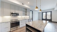 This thoughtfully designed single-floor residence blends contemporary finishes with functional living spaces. The open-concept kitchen serves as the heart of the home, showcasing a large center island with a striking blue-grey base topped with speckled granite countertops, illuminated by elegant brass pendant lights. White shaker-style cabinetry lines the walls, complemented by a classic subway tile backsplash and a full suite of stainless steel appliances, including a French door refrigerator, electric range, built-in microwave, and dishwasher. Warm-toned hardwood flooring flows throughout the main living areas, creating a cohesive and inviting atmosphere.

The bedrooms are bright and airy, each featuring large windows with exterior views that allow abundant natural light, along with ceiling fans and clean white walls. The bathrooms are finished to a high standard, with granite-topped grey vanities, large format tile flooring, white subway tile surrounds, and framed mirrors with modern wall sconces. Distinctive paneled interior doors in a deep charcoal tone add a bold, contemporary accent throughout the space. Overall, the residence offers a refined aesthetic that balances modern design with everyday comfort.