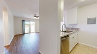 This well-appointed single-floor residence offers a clean, modern aesthetic throughout its thoughtfully designed layout. The open living area is anchored by warm hardwood-style flooring, a ceiling fan, and a sliding glass door that floods the space with natural light and provides direct access to a private outdoor patio. Wall-mounted accent lighting adds a welcoming ambiance to the living space.

The galley-style kitchen is efficiently designed with white shaker cabinetry, granite-look countertops, a stainless steel undermount sink, and a full suite of stainless steel appliances including a gas range, dishwasher, microwave, and refrigerator. Neutral tile flooring completes the kitchen's clean, functional look.

The bedrooms continue the hardwood-style flooring and feature ceiling fans, generous closet space, and sliding glass doors opening to the outdoor area, ensuring natural light and ventilation throughout. The space includes two bathrooms: a full bathroom with white cabinetry, granite countertops, and a shower/tub combination, and a secondary bathroom finished with tile flooring and a shower/tub unit. Both bathrooms maintain a consistent, crisp white palette. Overall, the residence presents a bright, move-in-ready environment with cohesive finishes and functional design.