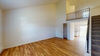 This two-floor residence offers a thoughtfully designed layout that balances open, airy living spaces with functional private retreats. The main level immediately impresses with its dramatic vaulted ceilings that soar upward, creating a sense of generous volume throughout the living area. Warm hardwood-style flooring runs consistently across the main floor, lending the space a cohesive and inviting character. A staircase with a sleek iron railing ascends to the upper level, which features an open loft-style overlook that adds architectural interest and visual connectivity between floors. The kitchen is well-appointed with white cabinetry, a subway tile backsplash, dark countertops, and a full suite of white appliances including a refrigerator, electric range, dishwasher, and a stainless steel sink. A closet with built-in shelving provides convenient storage adjacent to the main living area. Sliding glass doors on the main floor invite natural light and provide access to the exterior. The upper level transitions to plush carpeting and features a spacious bedroom with a ceiling fan and access to a walk-in closet. The bathroom offers natural light through a window with outdoor tree views. Baseboard heating is present throughout, and ceiling fans in key rooms enhance comfort. The overall ambiance is clean, bright, and move-in ready.