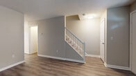 This three-floor property in Manchester, Connecticut presents a well-maintained layout with thoughtfully updated interiors throughout. The main living level features light-toned luxury vinyl plank flooring that flows through key areas, including a centrally positioned staircase with a white-painted banister that serves as an architectural focal point connecting the floors. Neutral gray wall tones complement the clean white trim and baseboards, creating a cohesive and modern aesthetic.

The kitchen is a functional highlight, equipped with white cabinetry featuring decorative arched detailing, granite-look countertops, a white subway tile backsplash, and stainless steel appliances including a range and dishwasher. Natural light enters through multiple windows fitted with blinds, and a door provides convenient exterior access directly from the kitchen.

The bedrooms are finished with plush carpet and offer natural light through standard windows, with baseboard heating units present throughout. A full bathroom features a tub-shower combination, white vanity cabinetry, and vinyl plank flooring, while an additional water closet provides added convenience.

The unfinished basement level offers a generously sized open space with a painted concrete floor and exposed wood-framed ceiling, presenting excellent potential for storage or future finishing.
