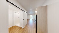 Located at 3417 Harbor Ave SW in Seattle's West Seattle neighborhood, Unit 223 is a thoughtfully designed one-bedroom, one-bathroom residence that maximizes every inch of its compact footprint. The open layout flows seamlessly from the kitchen through to the bedroom, creating an efficient and comfortable living environment.

The kitchen is outfitted with light wood cabinetry, white quartz countertops, and a full suite of stainless steel appliances including a refrigerator, dishwasher, over-the-range microwave, and a cooktop with a single basin sink — offering everything needed for daily cooking in a streamlined package.

Warm-toned luxury vinyl plank flooring runs throughout the entire unit, contributing to a bright, cohesive aesthetic. Recessed lighting illuminates the main living area, while clean white walls keep the space feeling open and airy.

A standout architectural detail is the sliding black barn door that provides access to the bathroom, adding a modern industrial touch. The bathroom features wood-toned cabinetry with a white countertop vanity, a walk-in shower, and warm flooring consistent with the rest of the unit.

The bedroom benefits from a large floor-to-ceiling window that fills the room with natural light and offers views of the surrounding neighborhood. This unit combines contemporary design with practical functionality in a prime Seattle location.