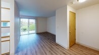 This single-floor unit is thoughtfully laid out, offering a clear and practical flow between its main living spaces. The living area is a standout feature, showcasing medium-toned wood-look flooring and a full sliding glass door that fills the room with natural light and provides direct views of a landscaped green outdoor area. A warm-toned interior door anchors one corner, adding a consistent wood accent carried throughout the unit.

The kitchen is efficiently designed in a U-shaped configuration, featuring white cabinetry with warm wood-toned trim, laminate countertops, and light wood-look flooring. It includes essential appliances—a refrigerator, range, and dishwasher—alongside ample upper and lower cabinet storage and a double sink.

A hallway connects the main living spaces to the bedroom and bathroom. The bedroom is finished with plush carpet flooring and benefits from a window that admits natural light. The full bathroom is neatly appointed with light wood-look flooring, a single-sink vanity with mirror and storage, a toilet, and a tub-shower combination with a curved curtain rod. Throughout the unit, white walls, flush-mount ceiling lighting, and consistent wood-tone accents contribute to a clean, functional, and cohesive overall aesthetic.