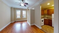 Located at 5254 S Dorchester Ave in Chicago's Hyde Park neighborhood, this single-floor unit offers a functional and well-maintained layout. The main living area features warm hardwood flooring that extends throughout, crown molding along the ceiling, and a ceiling fan with integrated lighting. Two windows allow natural light to fill the space, complemented by a baseboard heating system along the exterior wall. The open sightline into the kitchen creates a connected, airy feel.

The kitchen is efficiently designed with warm-toned wood cabinetry offering ample storage above and below the counter. Stone-look laminate countertops wrap the perimeter in an L-shaped configuration, housing a stainless steel sink and a white gas range. Tile flooring grounds the kitchen area, distinguishing it from the adjacent living space.

The bathroom features floor-to-ceiling white tile surrounding a soaking tub with an overhead shower. A privacy window above the tub allows natural light while maintaining seclusion. The vanity includes a built-in sink, and diamond-pattern tile flooring adds subtle visual interest. The overall ambiance of the unit is clean, neutral, and move-in ready.