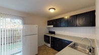 This three-floor home offers a straightforward, functional layout across its levels. The kitchen is a notable feature, equipped with bold dark cabinetry that contrasts with light grey laminate countertops and a white tile backsplash. The space includes a gas range, dishwasher, refrigerator, and a stainless steel sink, all set atop durable tile flooring. Ample upper and lower cabinet storage adds practicality to the room.

The main living area is carpeted and receives natural light through windows, creating a bright and open feel. A staircase with a metal railing connects the floors, contributing to the multi-level character of the home. The carpeted bedrooms are generously sized, each featuring neutral walls, standard ceiling vents, and windows that allow natural light to filter in.

Two bathrooms serve the home. One is a full bath with a tub-shower combination, white tile surround, tile flooring, a vanity with a white countertop, and dark cabinetry. The second is a half bath with similar finishes. The basement level houses the mechanical systems, including a water heater and furnace, and offers additional utility space with a painted concrete floor and exposed ceiling joists.