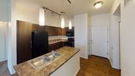 Located at 5000 N Mall Way in Flagstaff, Arizona, this single-floor unit offers a well-designed layout with a cohesive, contemporary aesthetic throughout. The kitchen serves as a central highlight, featuring rich dark-stained cabinetry that extends to the ceiling for ample storage, granite-style countertops, and a peninsula island with a double-basin sink. Pendant lighting and adjustable track lighting illuminate the space, while black appliances — including a refrigerator, range, and microwave — complete the kitchen's bold, modern look. Wood-style flooring runs through the kitchen and living areas, adding warmth and continuity. The bedrooms are carpeted and bright, each benefiting from natural light through windows. One bedroom includes a sliding mirrored closet door. The two bathrooms maintain the same design language as the kitchen, with dark wood vanities, granite-topped counters, and wood-style flooring. One bathroom features a shower-tub combination with clean white tile surround. A dedicated laundry area with a full-size side-by-side washer and dryer adds everyday convenience. The overall ambiance is clean, functional, and inviting, making this Flagstaff residence a practical and attractive living space.