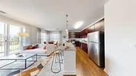 Located at 8501 Franklin Square Dr in Baltimore, MD, this 2-bedroom, 2-bathroom residence offers a thoughtfully designed open-concept floor plan that maximizes both space and functionality. The kitchen is a standout feature, showcasing rich dark-wood cabinetry, granite countertops, stainless steel appliances, and a central island with bar seating — ideal for casual dining or entertaining. Warm hardwood-style flooring flows seamlessly through the kitchen and living areas, adding a cohesive and inviting feel throughout.

The living room is generously sized, filled with natural light from large sliding glass doors that open to a private balcony with outdoor views. Adjacent to the living area, the dining space benefits from oversized windows dressed with elegant floor-to-ceiling curtains, creating a bright and welcoming atmosphere.

The primary bedroom is spacious and serene, featuring plush carpeting and a closet, offering a comfortable retreat. The second bedroom is equally well-proportioned with similar finishes. Both bathrooms are finished with granite-topped dark wood vanities and refined tilework, reflecting the same quality seen throughout the home.

Clean white walls, consistent modern finishes, and an abundance of natural light give this residence a polished, contemporary character throughout.