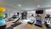 Located at 160–180 N Martin Luther King Blvd in Lexington, Kentucky, this single-floor fitness center is comprehensively outfitted to support a wide range of workout routines. The space is finished with patterned carpet tiles and recessed lighting throughout, creating a clean and functional environment.

The cardio zone is well-stocked with multiple TRUE-brand treadmills, elliptical trainers, and a stair climber, all positioned near windows fitted with horizontal blinds that allow natural light to fill the room. Wall-mounted flat-screen televisions are strategically placed throughout the space, providing entertainment during workouts.

A dedicated strength training area features a multi-functional cable machine suitable for a variety of resistance exercises, along with adjustable weight benches and rubber floor mats. A tiered dumbbell rack holds a full range of free weights, complemented by a set of medicine balls and a collection of stability and exercise balls in multiple sizes, catering to functional fitness and flexibility training.

Full-length mirrors line one wall, visually expanding the space while allowing users to monitor their form. A built-in water fountain with a bottle-filling station ensures convenient hydration. A posted workout guide on the wall adds an instructional element to the space. The overall layout is open and thoughtfully organized, offering ample room to move freely between equipment zones.