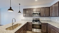 Located at 290 Jr Achievement Dr in Elkhart, Indiana, this single-floor residence offers a thoughtfully designed layout that balances functionality with modern style. The kitchen is a standout feature, showcasing rich dark-toned cabinetry with sleek hardware, light granite countertops, a subway tile backsplash, and a full suite of stainless steel appliances including a gas range, built-in microwave, and refrigerator. Pendant lighting adds a contemporary touch over the granite-topped peninsula, which also features an undermount sink. Wood-look flooring runs throughout the space, providing warmth and visual continuity across all areas. The living area is bright and open, benefiting from natural light that streams in through French doors leading to an outdoor balcony, complemented by a ceiling fan overhead. Additional rooms offer clean, neutral walls and generous proportions, providing versatile living space. The bathroom is well-finished, featuring a glass-enclosed walk-in shower, a granite-topped vanity with an undermount sink, a dark-framed mirror, and wood-look flooring that ties seamlessly to the rest of the unit. Overall, the space presents a clean, contemporary aesthetic with quality finishes throughout.