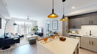 Located in Palm Beach Gardens, FL, this thoughtfully designed 2-bedroom, 2-bathroom residence offers a comfortable and contemporary single-floor layout. The open-concept kitchen, dining, and living area serves as the heart of the home, featuring light wood-tone flooring throughout, crisp white walls, and abundant natural light. The kitchen is equipped with stainless steel appliances, two-tone cabinetry in warm wood and dark charcoal, a large white quartz island with seating, and striking black pendant lights with gold interiors. The living room flows seamlessly from the kitchen and opens to a private balcony through floor-to-ceiling sliding glass doors, offering views of the surrounding community. Ceiling fans are present in both the living area and bedrooms. The primary bedroom is a well-proportioned retreat with a ceiling fan, natural light from a large window, and access to a dedicated closet. Both bathrooms are finished with light tile flooring, granite-topped vanities, and glass-enclosed showers. The second bedroom provides comfortable accommodations with its own closet. Throughout the residence, the design maintains a clean, modern aesthetic with neutral tones and consistent finishes, creating a cohesive and inviting living environment.