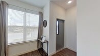 This contemporary multi-floor residence is designed with a clean, modern aesthetic, featuring crisp white walls, dark hardwood-style flooring, and abundant natural light throughout. The open-concept kitchen is a standout feature, equipped with white shaker cabinetry, stainless steel appliances including a French door refrigerator and range, a subway tile backsplash, and a large white island with seating for multiple bar stools — ideal for both cooking and casual dining.

The living area benefits from soaring ceilings and expansive floor-to-ceiling windows with a glass panel door, allowing generous natural light to fill the space. A large wall mirror enhances the sense of openness.

The bedrooms are well-proportioned, each featuring wide windows with horizontal blinds and drape panels that provide both light control and privacy. The bathrooms are finished with white vanities, wood-look flooring, and tub-shower combinations tiled in a striking marble-look pattern.

A dedicated laundry closet houses a stacked full-size washer and dryer, adding practical convenience. The entry area features a modern door with a sidelite window. Throughout, the residence maintains a cohesive, neutral palette with contemporary finishes.