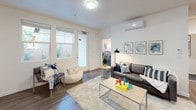 This single-floor residence is thoughtfully designed to accommodate multiple occupants, offering a functional and comfortable living environment throughout. The open living area serves as the heart of the unit, featuring durable wood-look flooring, large windows and a glass door that invite natural light and provide views of the surrounding greenery. A wall-mounted mini-split system ensures year-round climate comfort in this shared space.

The kitchen is well-equipped with rich, dark cabinetry, stainless steel appliances including a full-size refrigerator, dishwasher, microwave, and range, along with a double-basin sink and generous counter space — ideal for everyday meal preparation.

Each bedroom is carpeted in deep blue-grey tones and features its own wall-mounted mini-split climate control unit, offering individual comfort and privacy. The rooms provide ample space for a bed, desk, and storage, with windows in select rooms bringing in natural light.

The bathrooms are clean and functional, each featuring a full tub and shower combination with neutral finishes and wood-look flooring. The overall aesthetic throughout the residence is modern and understated, with light-toned walls creating a bright, welcoming ambiance suited to student or young professional living.