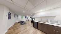 This fitness center offers a clean, modern environment designed to support a well-rounded workout routine. The space is finished with light hardwood-style flooring throughout, lending a bright and welcoming atmosphere that is complemented by recessed lighting and a grid-panel ceiling in portions of the room.

The cardio zone is a standout feature, housing multiple elliptical trainers, a stationary bike, and a treadmill — all from Life Fitness — arranged to maximize usability. A wall-mounted flat-screen television is positioned nearby for entertainment during workouts. A dedicated free-weight area includes a full dumbbell rack with a range of weights, accompanied by a workout mat and a flat bench for strength training exercises.

Motivational posters with themes such as "Focus," "Resilience," and "Growth" are displayed along one wall, adding an energizing visual element to the space. A ductless mini-split air conditioning unit ensures comfortable temperature control year-round, supplemented by baseboard heating.

A compact kitchenette along one wall features dark wood cabinetry with white upper cabinets, a stainless steel sink, and a mini-refrigerator — providing convenient access to hydration and post-workout refreshments. A mirrored wall section further enhances the sense of openness. Overall, this fitness center is a thoughtfully designed, fully functional space suited for daily exercise and wellness activities.