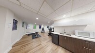 This fitness center offers a clean, modern environment designed to support a well-rounded workout routine. The space is finished with light hardwood-style flooring throughout, lending a bright and welcoming atmosphere that is complemented by recessed lighting and a grid-panel ceiling in portions of the room.

The cardio zone is a standout feature, housing multiple elliptical trainers, a stationary bike, and a treadmill — all from Life Fitness — arranged to maximize usability. A wall-mounted flat-screen television is positioned nearby for entertainment during workouts. A dedicated free-weight area includes a full dumbbell rack with a range of weights, accompanied by a workout mat and a flat bench for strength training exercises.

Motivational posters with themes such as "Focus," "Resilience," and "Growth" are displayed along one wall, adding an energizing visual element to the space. A ductless mini-split air conditioning unit ensures comfortable temperature control year-round, supplemented by baseboard heating.

A compact kitchenette along one wall features dark wood cabinetry with white upper cabinets, a stainless steel sink, and a mini-refrigerator — providing convenient access to hydration and post-workout refreshments. A mirrored wall section further enhances the sense of openness. Overall, this fitness center is a thoughtfully designed, fully functional space suited for daily exercise and wellness activities.