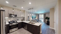 This well-designed single-floor residence offers a thoughtful open-concept layout that seamlessly connects the kitchen, dining, and living areas. The contemporary kitchen is a standout feature, showcasing two-tone cabinetry — light upper cabinets paired with dark lower cabinets — complemented by crisp white quartz countertops, stainless steel appliances including a gas range, microwave, dishwasher, and refrigerator, and a peninsula island with bar seating. Stylish pendant lighting hangs above the island, adding a modern touch. Wood-style plank flooring runs throughout the main living areas, enhancing the clean, cohesive aesthetic. The living room is bright and inviting, benefiting from a sliding glass door that opens to a private balcony with outdoor views. The bedroom is comfortably sized, featuring plush carpet, a ceiling fan, natural light from a large window, and direct access to a spacious walk-in closet. The full bathroom is finished with a backlit vanity mirror, dark wood cabinetry, quartz countertops, and a tub-shower combination. Recessed lighting throughout ensures consistent illumination across the entire space, creating a warm and functional living environment.