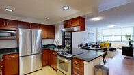 This single-floor residence offers a thoughtfully designed layout that maximizes functionality across its one-bedroom floor plan. The open-concept kitchen and living area serves as the heart of the home, seamlessly blending cooking, dining, and lounging spaces. The kitchen is outfitted with rich, warm-toned cabinetry, dark granite countertops, stainless steel appliances including a full-size refrigerator, dishwasher, and a slide-in range with overhead ventilation hood. A peninsula with additional counter space provides a practical division between the kitchen and the adjoining living area. Light bamboo-style hardwood flooring runs throughout the main living space, contributing to a bright, clean aesthetic. The living room benefits from large windows that allow natural light to fill the room, creating an airy and open atmosphere. The bedroom offers a comfortable and serene retreat, finished with plush carpeting, neutral-toned walls, and window treatments that provide privacy while allowing natural light. A dedicated closet provides practical storage. Overall, the space presents a modern, urban aesthetic with consistent finishes and a cohesive design throughout.