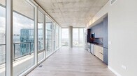 Located in the heart of Nashville's Midtown, this high-rise residence offers a striking contemporary design defined by soaring exposed concrete ceilings, light hardwood flooring, and an expansive wall of floor-to-ceiling glass that floods the interior with natural light. The open-concept living, dining, and kitchen area forms the centerpiece of the home, with panoramic views of the Nashville skyline serving as a dramatic backdrop. The sleek kitchen features stainless steel appliances, a full-height concrete-finish cabinetry wall, warm wood lower cabinets, and a built-in range, refrigerator, and dishwasher. A private balcony extends the living space outdoors, offering unobstructed elevated views of the downtown skyline, including neighboring high-rises. Both bedrooms are well-proportioned, each benefiting from floor-to-ceiling windows that frame city views and fill the rooms with daylight. The bathroom is finished with large-format tile flooring, modern floating vanities with integrated sinks, and clean, neutral tones throughout. A dedicated laundry area, multiple closets, and an entrance foyer complete the thoughtfully organized layout, making this a refined urban residence with impressive architectural presence.