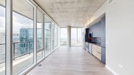 Located in the heart of Nashville's Midtown, this high-rise residence offers a striking contemporary design defined by soaring exposed concrete ceilings, light hardwood flooring, and an expansive wall of floor-to-ceiling glass that floods the interior with natural light. The open-concept living, dining, and kitchen area forms the centerpiece of the home, with panoramic views of the Nashville skyline serving as a dramatic backdrop. The sleek kitchen features stainless steel appliances, a full-height concrete-finish cabinetry wall, warm wood lower cabinets, and a built-in range, refrigerator, and dishwasher. A private balcony extends the living space outdoors, offering unobstructed elevated views of the downtown skyline, including neighboring high-rises. Both bedrooms are well-proportioned, each benefiting from floor-to-ceiling windows that frame city views and fill the rooms with daylight. The bathroom is finished with large-format tile flooring, modern floating vanities with integrated sinks, and clean, neutral tones throughout. A dedicated laundry area, multiple closets, and an entrance foyer complete the thoughtfully organized layout, making this a refined urban residence with impressive architectural presence.