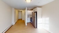This 260 square foot apartment in Derry, NH, offers a thoughtfully designed living space within a compact footprint. The single-floor layout maximizes functionality, featuring a well-appointed bathroom and a strategically placed hallway for easy navigation.

The bathroom boasts modern fixtures, including a white vanity with a sink, toilet, and a bathtub-shower combination. Light-colored walls and wood-look flooring create a clean, spacious feel. The hallway serves as a central artery, connecting various areas of the apartment efficiently.

The main living area is characterized by its bright, airy ambiance, enhanced by white walls and light wood-toned flooring. Baseboard heating units line the walls, ensuring comfort throughout the seasons. A large window allows natural light to flood the space, while offering views of the exterior.

The kitchen, though compact, is equipped with essential appliances including a refrigerator and stove. White cabinetry provides ample storage, complementing the overall color scheme of the apartment. The open concept design seamlessly integrates the kitchen with the living area, promoting a sense of spaciousness.

Despite its small size, this apartment effectively balances functionality and comfort, making it an ideal residence for individuals or couples seeking an efficient urban living space.