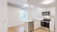 Located at 168 Wellington St in Kingston, Ontario, this efficiently designed one-bedroom, one-bathroom unit offers a thoughtfully arranged single-floor layout. Light hardwood flooring runs throughout, complementing the bright, neutral colour palette that gives the space an open and airy feel.

The kitchen is a standout feature, outfitted with crisp white shaker-style cabinetry, white quartz countertops, and a full suite of stainless steel appliances including a refrigerator, electric range, over-the-range microwave, and dishwasher. A double stainless steel sink is positioned beneath a window, allowing natural light into the cooking area. Exposed silver ductwork adds an industrial accent along the upper portion of the space.

The bedroom is a well-proportioned room with a window that brings in natural light, continuing the clean, minimal aesthetic found throughout the unit. White panelled doors with matte black hardware provide access to the bedroom, bathroom, and a closet, adding a refined contrast to the soft neutral walls.

The bathroom maintains the same clean, modern design with light flooring and white walls. The unit also includes an in-unit laundry area, adding everyday convenience. Overall, this space presents a functional, modern environment well-suited for comfortable urban living in downtown Kingston.