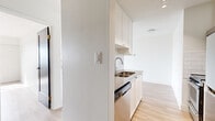 This well-appointed 1-bedroom, 1-bathroom residence offers a clean, modern aesthetic throughout, with light hardwood flooring and crisp white walls creating a bright, cohesive atmosphere. The living room is a standout space, anchored by expansive sliding glass doors that open onto a private balcony revealing impressive water and garden views — an ideal setting for relaxing or entertaining. The bedroom is a comfortable, well-proportioned room featuring a large mirrored sliding-door closet and a window that frames additional outdoor scenery, filling the space with natural light. The galley-style kitchen is efficiently designed, featuring white shaker cabinetry, a white subway tile backsplash, stone-toned countertops, a stainless steel double sink, and a full suite of stainless steel appliances including a refrigerator, stove, and dishwasher. The bathroom is finished with large-format floor tiles, a full soaking tub surrounded by white subway tile, a modern vanity with an undermount sink, and a wide mirror. A hallway connects the rooms, maintaining a logical and functional flow throughout. The space is characterized by its clean lines, abundant natural light, and serene outdoor views.