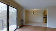 This single-floor unit offers a well-organized layout designed to maximize functionality within its thoughtfully arranged living space. The open living and dining area serves as the heart of the unit, featuring light hardwood-style flooring that extends throughout, contributing to a warm and cohesive aesthetic. A decorative chandelier anchors the dining area, adding a subtle touch of elegance to the otherwise clean, neutral interior.

Large sliding glass doors in the living area provide direct access to a private balcony, framing views of surrounding wooded scenery and allowing abundant natural light to fill the space. A wall-mounted HVAC unit and baseboard heating ensure year-round climate comfort. The neutral, warm-toned walls throughout create a versatile backdrop suitable for a variety of furnishing styles.

The unit includes one bedroom and one full bathroom, offering a straightforward and efficient floor plan. The overall ambiance is calm and inviting, enhanced by the natural views visible through the expansive glass door, making this a practical and pleasant single-floor living space.