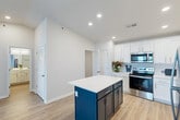 Located at 270 Lancer Drive in Nicholasville, Kentucky, this well-appointed one-bedroom, one-bathroom residence offers a thoughtfully designed single-floor layout with a clean, contemporary aesthetic throughout. The open kitchen is a standout feature, showcasing white shaker-style cabinetry, bright quartz countertops, and a striking navy blue center island with a white countertop. A full suite of stainless steel appliances—including a refrigerator, range, microwave, and dishwasher—completes the space, all set atop light wood-look luxury vinyl plank flooring. The living area is bathed in natural light and features a ceiling fan and French doors that open directly onto a private balcony, offering pleasant outdoor views. The generously sized bedroom is finished with soft wall-to-wall carpeting, a broad window with blinds for natural light, and access to a dedicated closet. The bathroom connects conveniently to both the bedroom hallway and main living areas, while a separate laundry room houses a full-size side-by-side Whirlpool washer and dryer. Neutral wall tones, recessed lighting, and consistent flooring choices give the entire space a cohesive, move-in-ready feel.