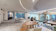 Located at 329 Alfred Ave in Teaneck, NJ, this single-floor commercial space offers a thoughtfully designed, contemporary work environment that balances open collaboration with private functionality. The layout includes four distinct zones, each suited to different working styles and needs.

The open collaborative area is the heart of the space, featuring a mix of modular seating arrangements, light-toned furniture, and a dynamic contrast between patterned carpet tiles and warm hardwood flooring. Curved LED light strips trace elegant paths across the white ceiling, adding an architectural focal point while providing consistent, ambient illumination throughout.

Glass-partitioned enclosed rooms line the perimeter, offering visual transparency while maintaining acoustic separation. These private areas are equipped with built-in desks and large windows that invite abundant natural light and garden views. Black-framed glass sliding doors add a refined industrial touch to the overall aesthetic.

A standout feature near the stairwell landing is a dramatic full-height marble accent wall with bold gold veining, anchoring the transitional zone between the open floor and the enclosed rooms. The stairwell itself incorporates glass balustrades, reinforcing the space's commitment to transparency and light.

Throughout, the design achieves a polished, professional ambiance with a modern sensibility, making it well-suited for a collaborative and productive office environment.