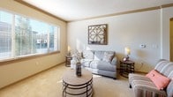 This thoughtfully designed single-floor residence offers a cohesive, comfortable layout across several well-defined living spaces. The kitchen serves as a functional centerpiece, featuring warm medium-toned wood cabinetry that extends to the ceiling, dark granite countertops, stainless steel appliances, recessed and pendant lighting, and a central island with bar seating — ideal for both cooking and casual dining. Wood-look flooring runs throughout the kitchen, adding warmth and durability.

The adjacent dining area provides a dedicated space for formal meals, with neutral walls and tile flooring that complement the overall palette of the home. The living room benefits from generous natural light streaming through large windows with horizontal blinds, plush carpet underfoot, crown molding, and a relaxed, open feel.

The primary bedroom is generously proportioned, featuring soft carpet, exposed beam detailing on the ceiling, a window overlooking the exterior, and flanking nightstands with matching lamps. A second bedroom offers a bright, sunlit atmosphere with a wide horizontal window and direct access to a built-in closet with shelving. Both bathrooms are well-equipped, each showcasing dark granite vanity tops, wood cabinetry, and wood-look tile flooring. One bathroom includes a tub-shower combination, while the other offers a sleek, elongated vanity with a large mirror.