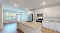 Located at 2620 Mall of Georgia Blvd in Buford, GA, this single-floor residence offers a thoughtfully designed open-concept layout filled with contemporary finishes. The kitchen serves as the centerpiece of the living area, showcasing a large granite-topped island with an undermount sink, white shaker-style cabinetry extending to the ceiling, and a full suite of stainless steel appliances including a refrigerator, electric range, and built-in microwave. A tile backsplash adds a refined touch, while light hardwood-style flooring flows throughout the main living areas, creating a warm, cohesive aesthetic. The living area is bathed in natural light from generously sized windows that frame views of lush greenery outside. Bedrooms feature plush carpeting, ceiling fans, and large windows that continue the bright, airy feel of the space. Ample storage is provided through spacious closets equipped with wire shelving systems. The bathroom is finished with granite countertops, white cabinetry, and clean tile work, maintaining the consistent modern style found throughout the unit. Recessed lighting and crisp white walls contribute to an overall ambiance that is bright, clean, and move-in ready.