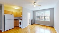 Located in Chicago's vibrant Lakeview neighborhood, this compact yet functional unit at 910 West Dakin Street offers a well-organized layout across a single floor. Warm hardwood flooring runs throughout the space, lending a classic and cohesive feel to the interior. The main living area is bright and open, illuminated by a ceiling fan with a light fixture and a sizeable window that invites natural light while offering views of the surrounding residential streetscape. A cast-iron radiator beneath the window provides traditional heating. The kitchen is neatly tucked into a defined alcove, featuring light wood cabinetry, tile backsplash, a gas range, full-size refrigerator, and a sink — offering all essential amenities in an efficient footprint. A dedicated sleeping area includes a mirrored sliding closet door, adding depth and storage to the room. The full bathroom is finished in clean white tile, complete with a tub-shower combination, pedestal-style vanity, medicine cabinet mirror, and a frosted privacy window. The unit's straightforward layout and classic finishes make it a practical and comfortable Chicago residence.