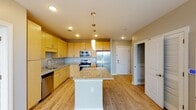 Located at 1709 Cresthill Ave in Royal Oak, Michigan, this single-floor residence offers a thoughtfully designed layout with modern finishes and an open, airy feel throughout. The kitchen serves as a central highlight, featuring warm honey-toned cabinetry, granite countertops, a large center island with pendant lighting, and a full suite of stainless steel appliances including a refrigerator, range, microwave, and dishwasher. Light hardwood flooring runs throughout the main living areas, enhancing the bright and welcoming atmosphere. The living area is generously proportioned, with floor-to-ceiling sliding glass doors that open to a balcony overlooking the Royal Oak cityscape, allowing abundant natural light to fill the space. The bedroom is carpeted for comfort and features a large window with sweeping urban views. A spacious walk-in closet with built-in wire shelving provides ample storage. The primary bathroom is well-appointed with a dual-sink granite vanity, light wood cabinetry, and a tiled walk-in shower with modern fixtures. A secondary bathroom mirrors the same refined aesthetic. Neutral gray tones on the walls complement the light flooring and finishes, creating a cohesive and contemporary living environment throughout the residence.