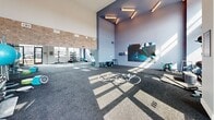 Located at 430 Englewood Ave SE in Atlanta, GA, this dynamic two-story fitness center offers an impressive and well-appointed workout environment. The main floor commands attention with soaring double-height ceilings and a wall of large windows that flood the space with natural light and frame outdoor views. This level houses a robust cardio zone with treadmills, stair climbers, and rowing machines, alongside a dedicated strength training area featuring cable machines, free weights, and functional training rigs. A standout open functional training studio features rubber flooring, battle ropes, kettlebells, and a large display screen, anchored by a bold logo graphic on the floor. Vibrant, large-scale murals throughout add an energetic, community-driven aesthetic, complemented by motivational signage. The upper level, accessible by staircase, offers an intimate mezzanine space equipped with air bikes, a stair climber, and additional functional training equipment. Patterned accent walls and an open railing overlooking the main floor give this level a distinct character. Hardwood-style flooring with teal accent striping ties the design together, while ample overhead lighting ensures a bright and welcoming atmosphere throughout the entire facility.