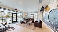 Located at 1310 E St. Louis Street in Springfield, Missouri, this single-floor lounge space offers a compact yet well-appointed layout with a distinctive aviation-inspired design aesthetic. The space is anchored by a dramatic large-scale vintage aircraft mural that commands one full wall, paired with bold track lighting reminiscent of stage or hangar fixtures, reinforcing the "Hangar" theme carried throughout the interior.

Light wood-look flooring runs throughout, complementing the clean white walls and lending a contemporary feel. The front of the space features expansive floor-to-ceiling black-framed windows and a glass entry door that flood the interior with natural light and provide clear views of the surrounding streetscape. This glazed facade creates an open, welcoming atmosphere from the moment of entry.

The seating area is furnished with rich brown leather sofas and a wood coffee table, arranged atop a layered area rug for a comfortable lounge setting. Toward the rear, a dedicated dining area with a round wood table and modern chairs sits atop a cowhide rug, accompanied by a built-in wet bar with dark wood cabinetry, open shelving, a beverage refrigerator, and a wall-mounted flat-screen TV. Recessed and track lighting throughout ensures the space is well-lit at all hours. Decorative elements including a large wall clock, vintage trunks, and framed artwork complete the cohesive, industrial-chic hangar theme.
