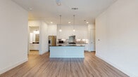 Located at 10400 Research Blvd in Austin, TX, this thoughtfully designed one-bedroom residence offers a well-appointed, single-level layout with a clean, modern aesthetic throughout. The open-concept kitchen and living area serves as the heart of the home, featuring crisp white shaker cabinetry extending to the ceiling, dark quartz countertops, a stylish penny-tile backsplash, stainless steel appliances including a French door refrigerator and electric range, and a central island — all set atop warm wood-look vinyl flooring. Large floor-to-ceiling windows and a glass door in the living area flood the space with natural light and offer views of the surrounding greenery. The dining area flows naturally from the kitchen, creating a cohesive, versatile entertaining space. The generously sized primary bedroom is finished with plush carpet, a ceiling fan, and a large window that brings in ample daylight. It connects directly to a spacious walk-in closet equipped with dual hanging rods and built-in shelving. A dedicated laundry room with in-unit washer and tile flooring adds everyday convenience. Neutral wall tones and clean lines throughout give the space a bright, contemporary feel.