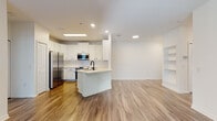 This single-floor residence offers a thoughtfully designed open-concept layout that seamlessly connects the kitchen and living area. The kitchen is equipped with stainless steel appliances, including a refrigerator, range, and over-the-range microwave, all set against crisp white cabinetry with black hardware and a white subway tile backsplash. A central island with a stainless steel sink and light countertops provides additional workspace and casual dining. Warm wood-look flooring flows throughout the main living areas, complemented by recessed lighting and a ceiling fan overhead. Built-in shelving adds a functional design element to the living space, which also benefits from access to natural light through window-fitted exterior doors. The bedrooms feature plush carpet flooring, ceiling fans, and windows with blinds that allow for natural light and privacy. Both bathrooms are finished with white cabinetry, light countertops, black hardware accents, and tiled tub-shower combinations set on wood-look flooring. A dedicated laundry room with a full-size washer and dryer adds everyday convenience. The overall aesthetic is clean, modern, and move-in ready.